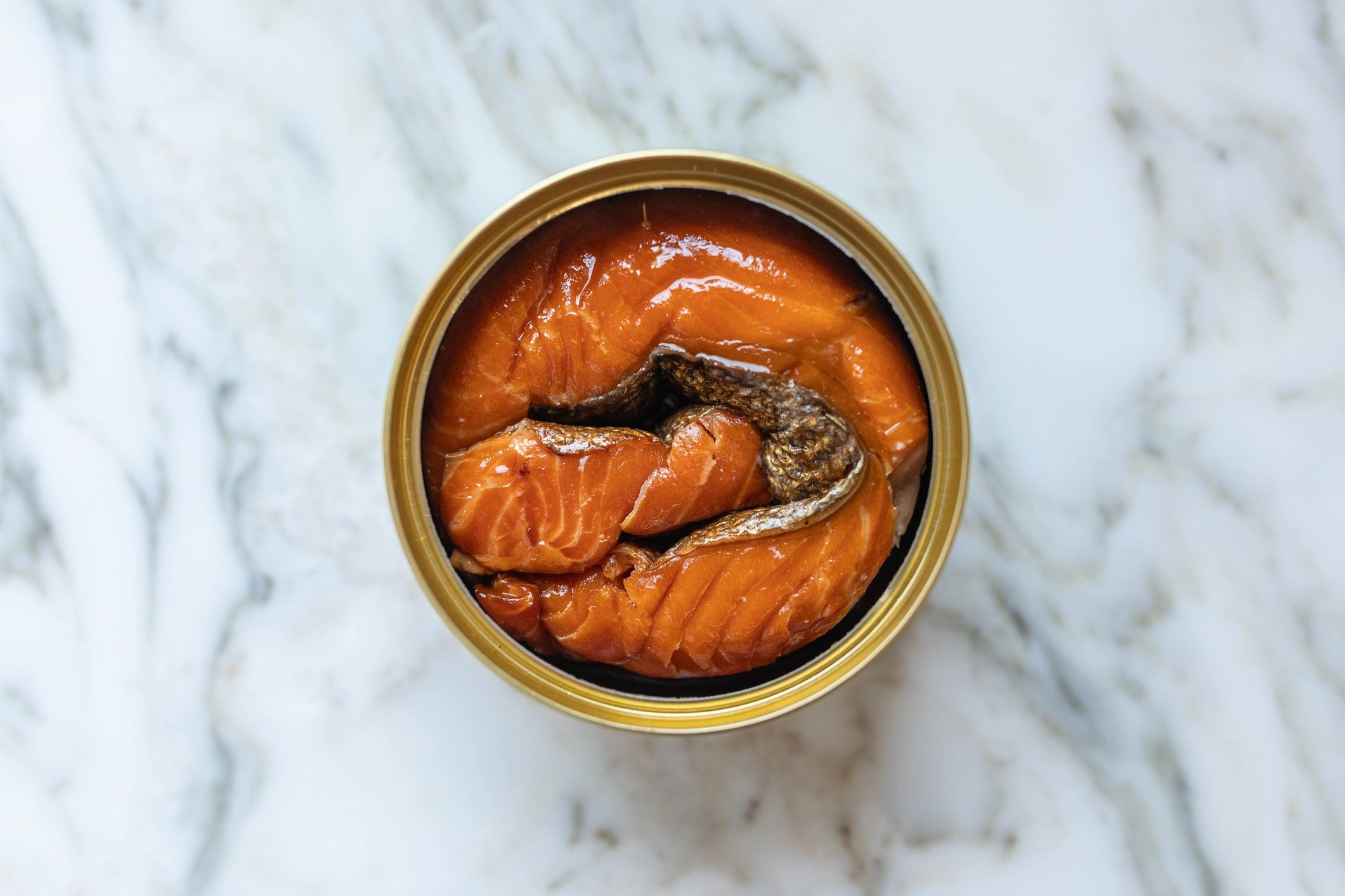 Top-down view of an open tin of preserved salmon on a light surface